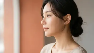 A close-up profile of a woman with flawless, smooth skin surrounded by a warm, soft terracotta and light gray aesthetic.