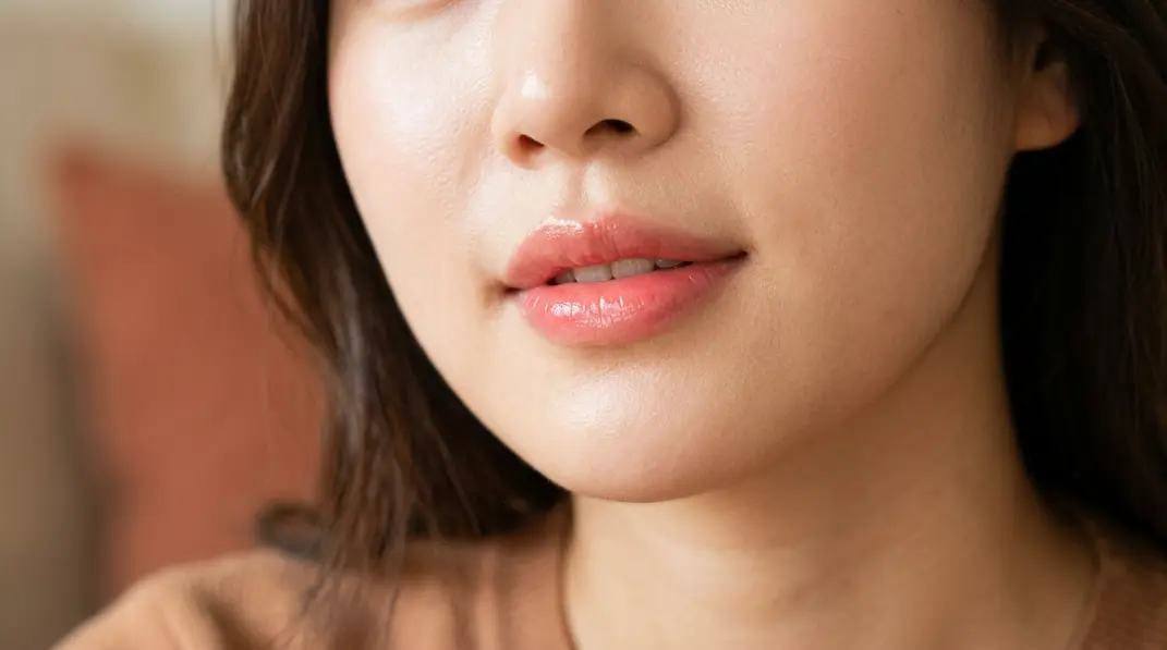 A detailed close-up of beautifully natural, clear, glossy pinkish-coral lips reflecting Korean beauty aesthetics.